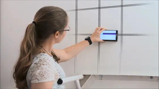 This young woman is showing how to use the WalabotDIY to locate steel reinforcing rods in a cast concrete wall. Photo credit: WalabotDIY