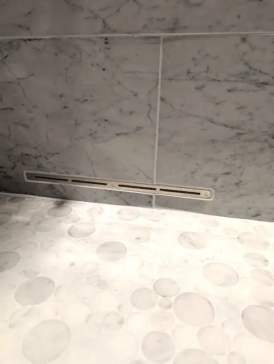 tile shower with a ventilation fan slot at the floor